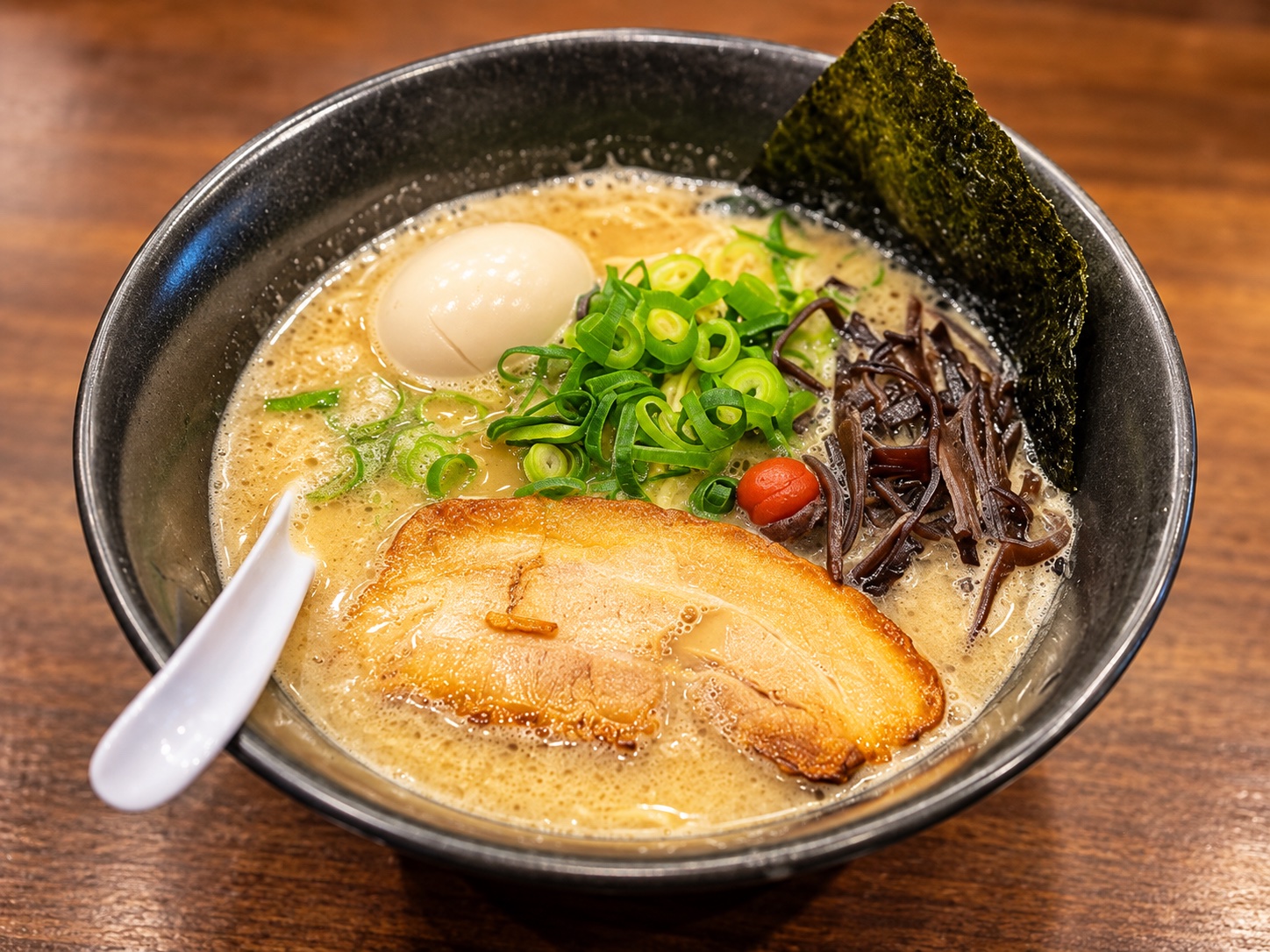 豚骨スープにチャーシュー、青ねぎ、きくらげ、味玉を添えた料理イメージの接写